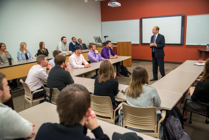 A guest speaker addresses Bethany Lutheran College students in a modern lecture room equipped with a projector and whiteboards.