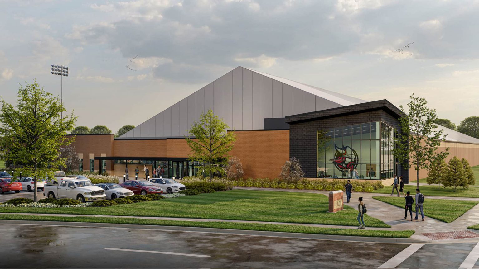 Bethany Lutheran Colleges modern sports complex features a distinctive large triangular roof and a glass entrance. Students and visitors can be seen walking near parked cars on a cloudy day.