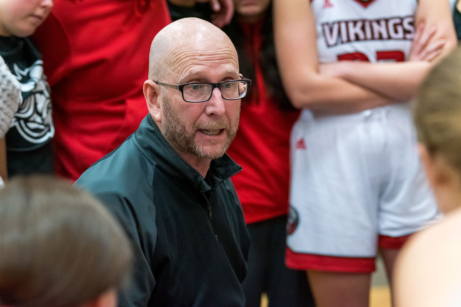 A coach addresses the Bethany Lutheran College womens basketball students, who are wearing red and white uniforms.