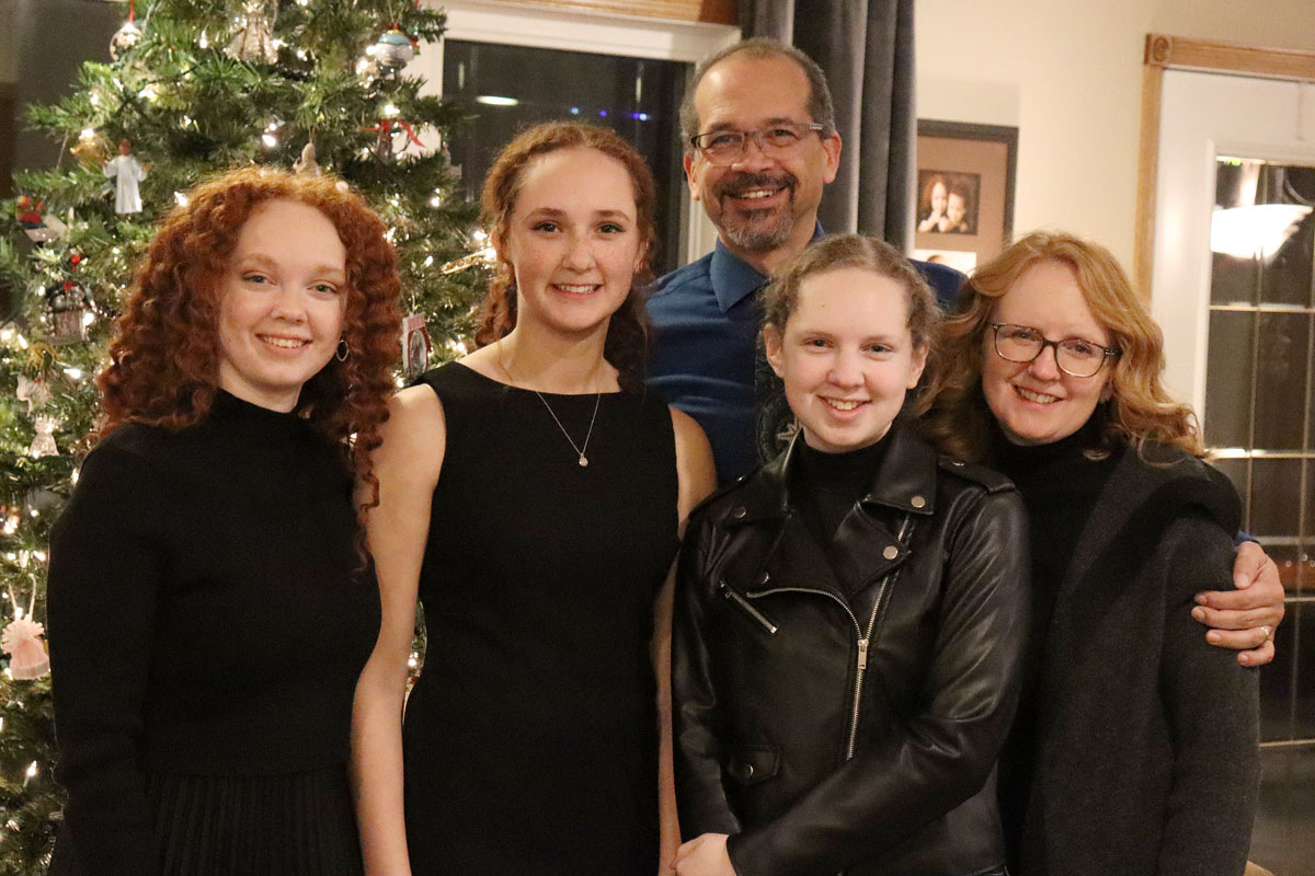 Five Bethany Lutheran College students pose together in front of a decorated Christmas tree inside a home.