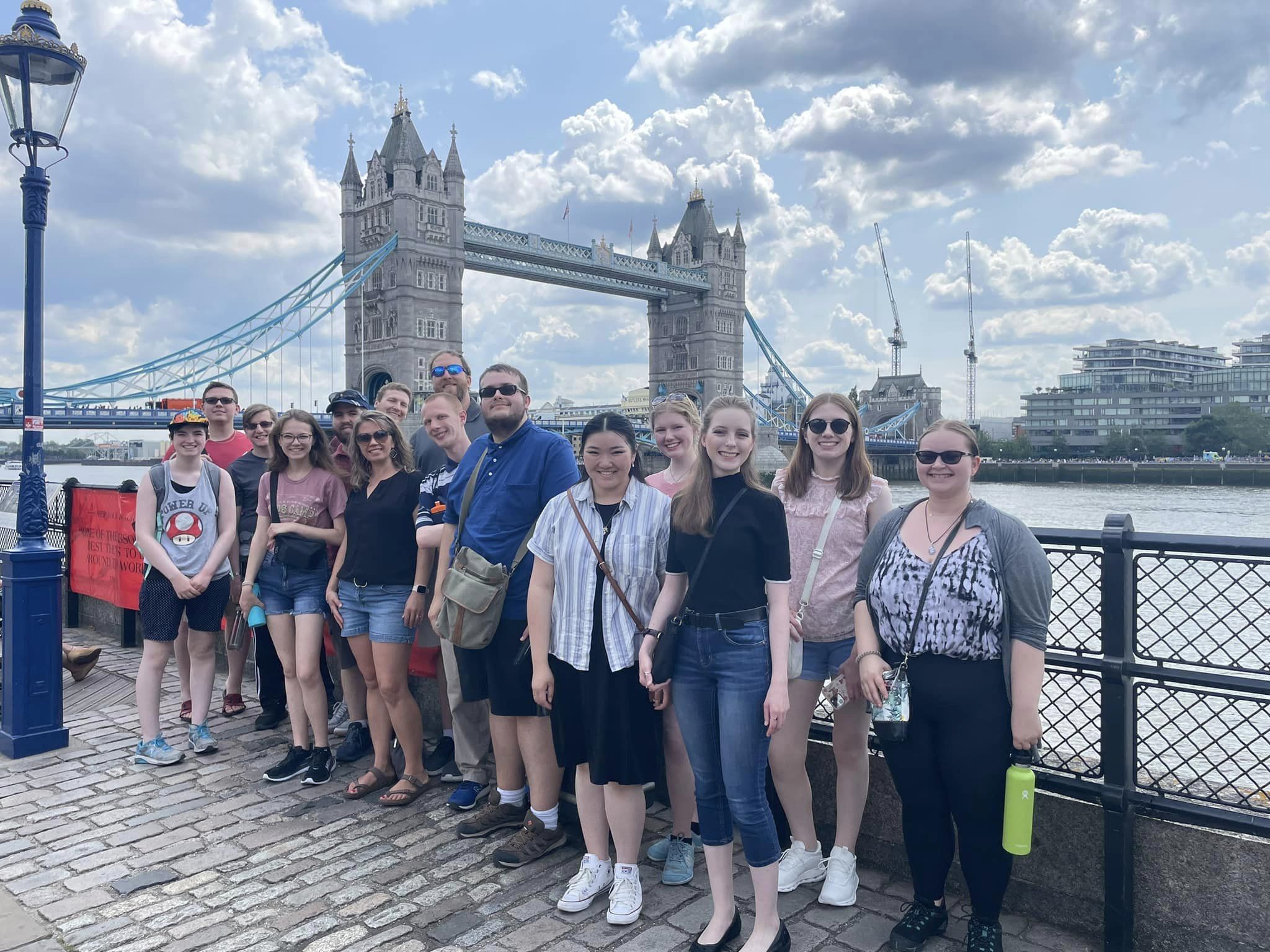 A group of Bethany Lutheran College students posing in front of Londons Tower Bridge on a partly cloudy day.