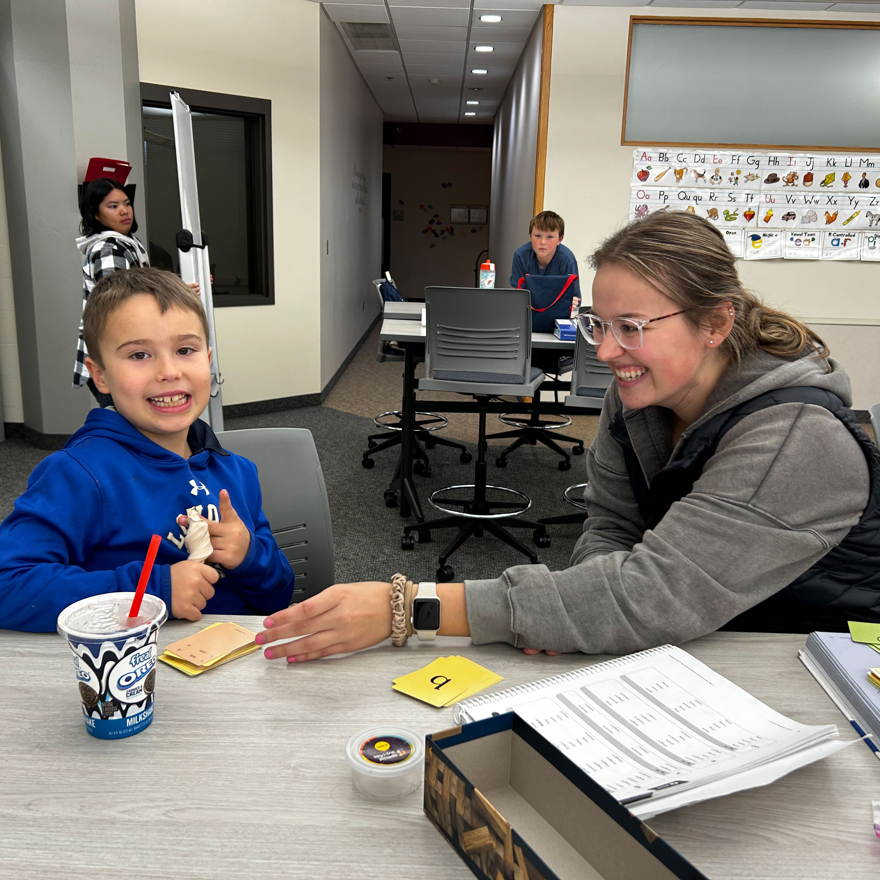 A student and a teacher engage in a learning activity at Bethany Lutheran College, sitting together with educational materials and a drink in a classroom environment.