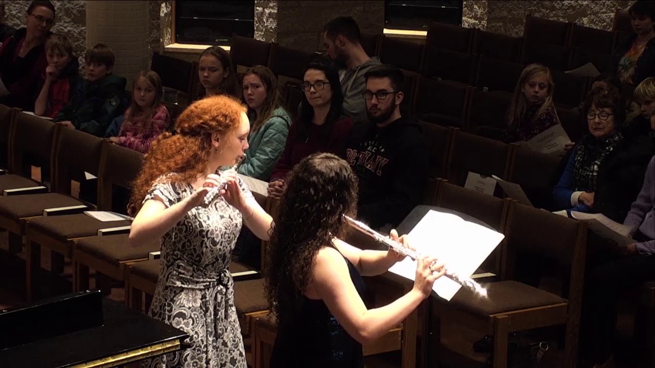 Two women play the flute at Bethany Lutheran College in Mankato, performing in front of an audience seated in church pews.
