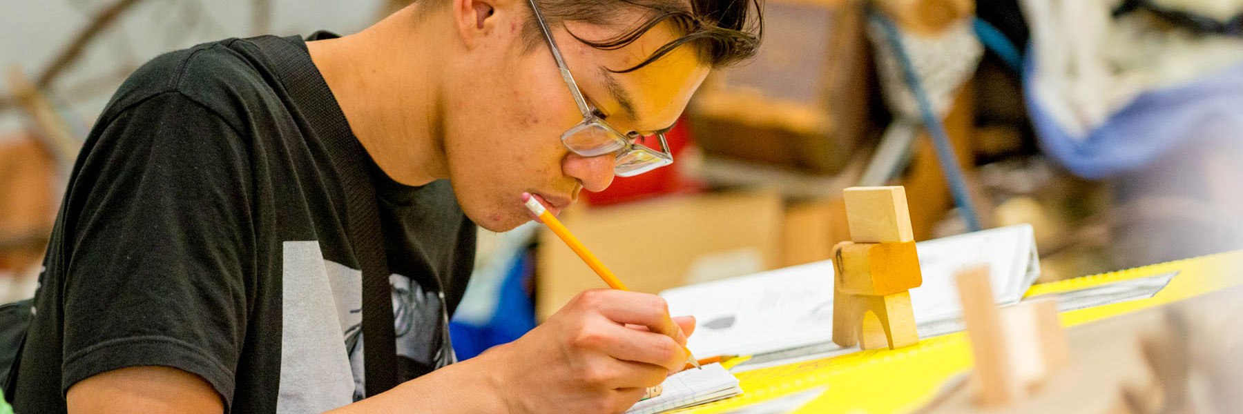 A student wearing glasses writes with a pencil at a desk, reviewing notes at Bethany Lutheran College.