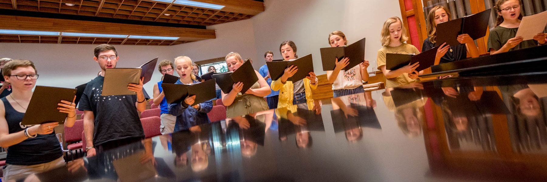 A group of young adults in Mankato sing from sheet music during an indoor campus community choir rehearsal.