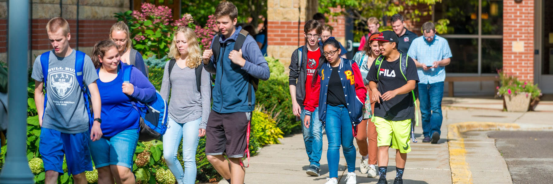 A group of students walks together on a sunny sidewalk at Bethany Lutheran College, with greenery in the background.