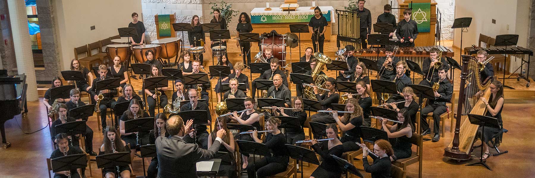 A large orchestra performs on a church stage at Bethany Lutheran College, engaging the campus community with vibrant music.