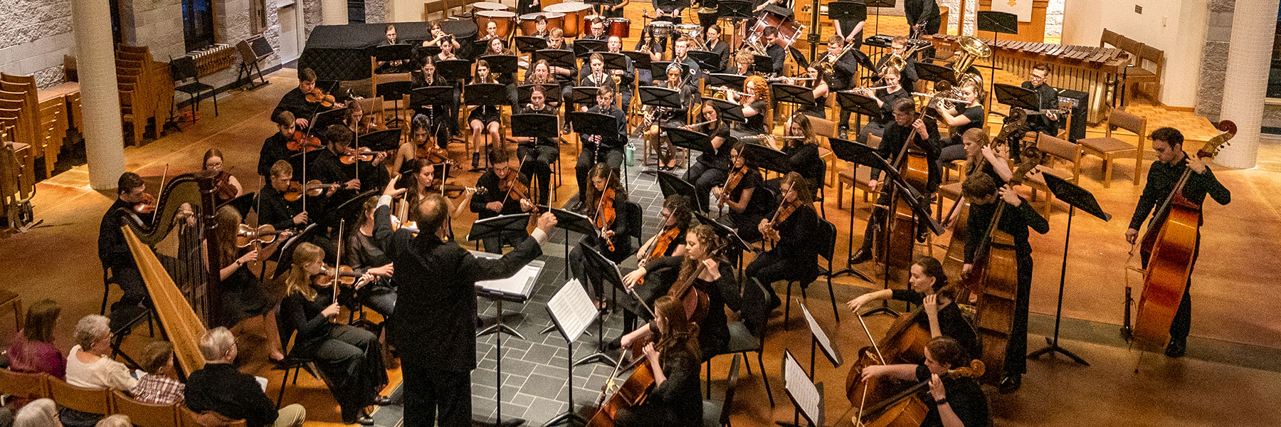 An orchestra performs on stage with a conductor in a Mankato concert hall, engaging members of the campus community.