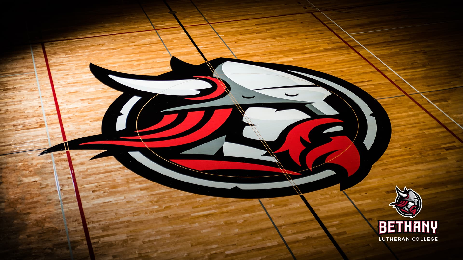 A Viking mascot logo positioned at the center of a gym floor represents Bethany Lutheran College and its Minnesota campus community.