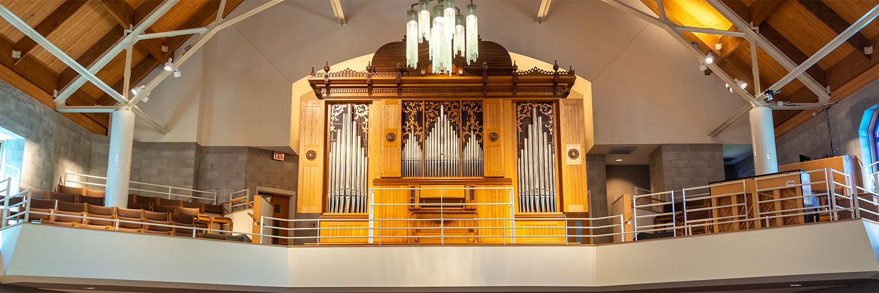 A large pipe organ with wooden accents is situated on a church balcony in Mankato, Minnesota, next to empty choir seats and a grand piano.