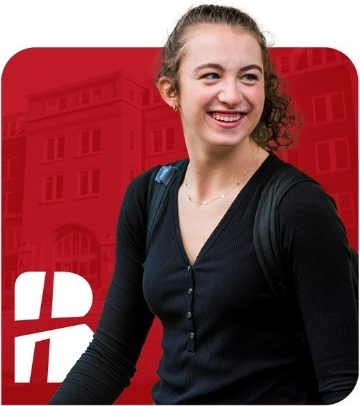 Smiling female college student with curly hair wearing a black top and backpack, standing in front of a red background featuring a faded academic building and white "B" logo.