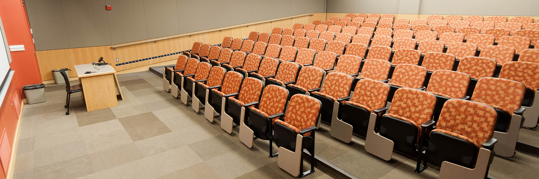 Empty lecture hall at Bethany Lutheran College in Mankato, Minnesota, featuring rows of orange patterned seats.
