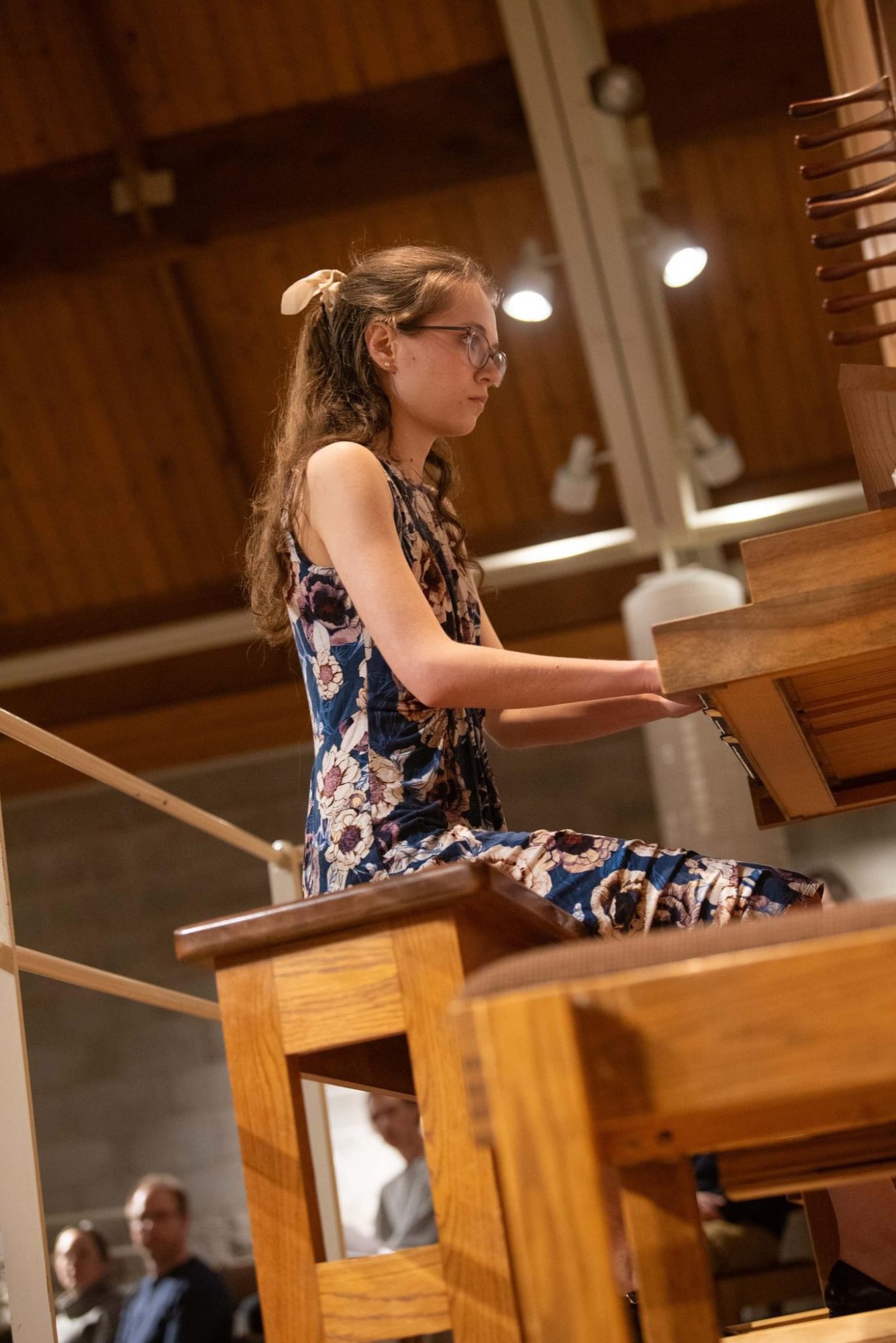 A Bethany Lutheran College student wearing a floral dress plays a wooden organ on stage to an attentive audience.