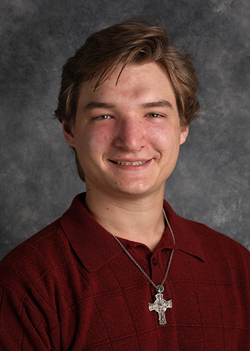 A smiling student with short light brown hair, wearing a red polo shirt and a cross necklace, at Bethany Lutheran College in Mankato.