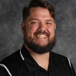 Aaron Mantey, Counselor for the Admissions Department, smiles while posing in front of a mottled gray background in Mankato, Minnesota.
