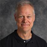 Andy Overn, Professor for the Graphic Design Department, stands in front of a textured gray background at Bethany Lutheran College.