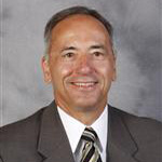 Art Westphal, Senior Development Officer for the Advancement Department, poses in front of a gray background.