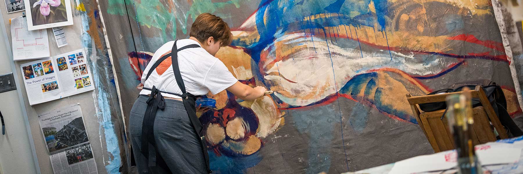 A Bethany Lutheran College student paints a vibrant abstract artwork in a cluttered studio, fostering campus community.