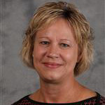 Barb Dressen, Executive Assistant of the President's Office Department, smiles in front of a gray background at Bethany Lutheran College.