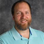 Ben Faugstad, Associate Professor for the Music Department, poses in front of a gray mottled background.