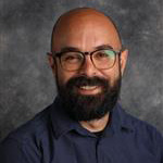 Ben Lundsten, Assistant Professor for the Media Arts Department, poses against a gray background.