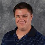 Benji Inniger, Adjunct Faculty for the Theatre Department, standing in front of a gray mottled background.