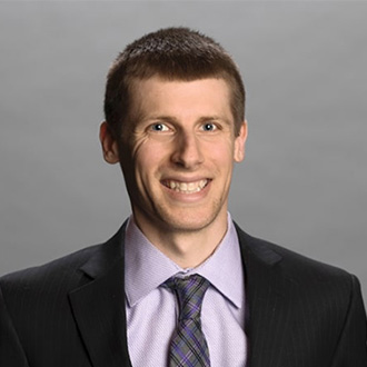 A smiling man with short brown hair, wearing a suit and tie, poses at Bethany Lutheran College in Minnesota.