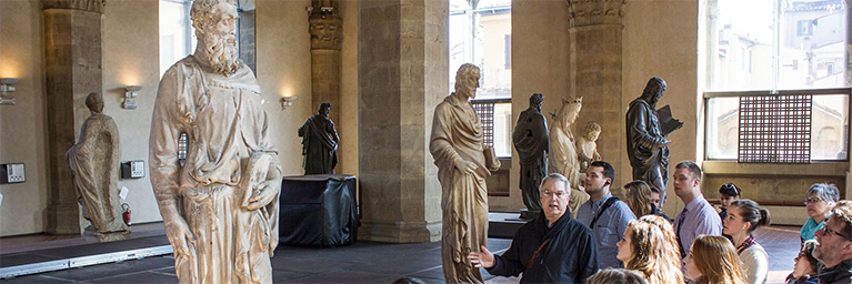 A tour guide engages a group of students in a Minnesota museum room containing large classical statues.