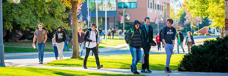 Students walk across the sunny Bethany Lutheran College campus in Minnesota, engaging with one another in a vibrant atmosphere.