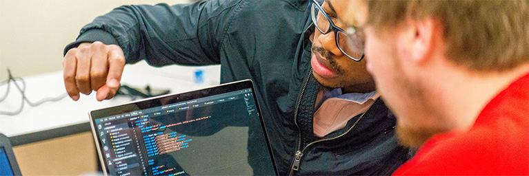 Two people in Mankato discuss programming as they look at code displayed on a laptop screen.