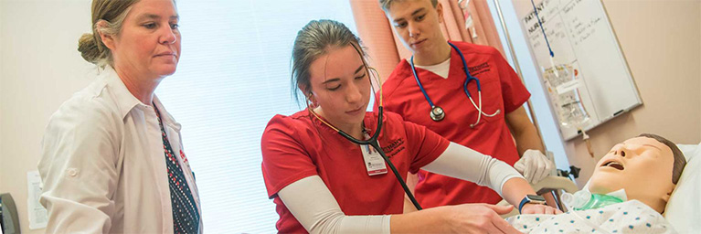Three healthcare workers practice a medical procedure on a mannequin at Bethany Lutheran College in Minnesota.
