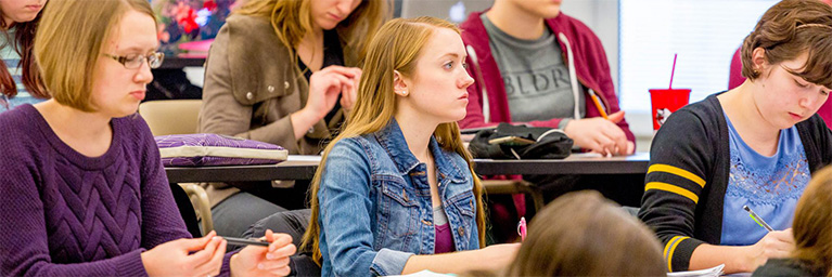 Students seated at desks in a Bethany Lutheran College classroom listen attentively and take notes during a lecture.