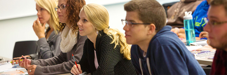 Students at Bethany Lutheran College in Mankato sit at desks, attentively listening and taking notes during class.