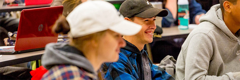 Students wearing casual clothes and hats smile and listen attentively during a class at Bethany Lutheran College in Mankato.