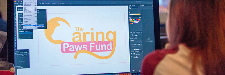 A person at Bethany Lutheran College uses graphic design software to create a Caring Paws Fund logo featuring a cat graphic.