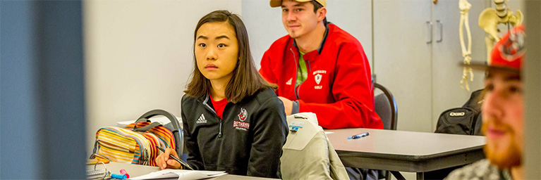Students seated at desks in a Minnesota classroom, engaged as they listen and take notes.