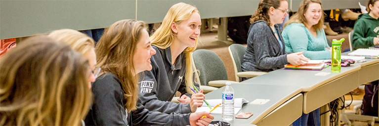 Students at Bethany Lutheran College sit at desks, smiling and conversing during an engaging classroom lecture.