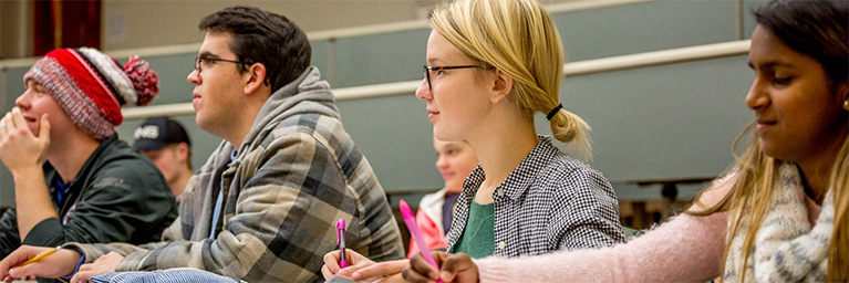 Students in a lecture hall at Bethany Lutheran College listen attentively and take notes, demonstrating student engagement.