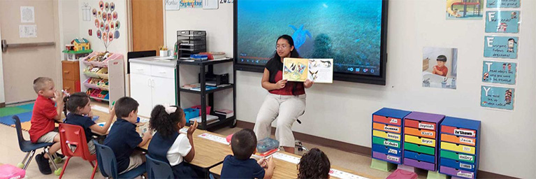 A teacher from Bethany Lutheran College reads to young students in a colorful classroom, fostering student engagement.