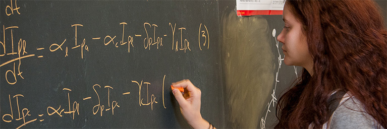A young woman at Bethany Lutheran College writes mathematical equations on a chalkboard using orange chalk.