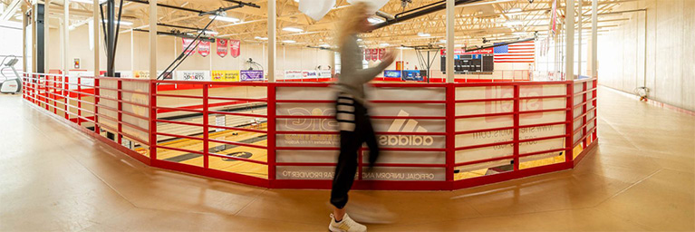 A person walks on an indoor track located above a gym with basketball courts, illustrating student activity within the campus community.