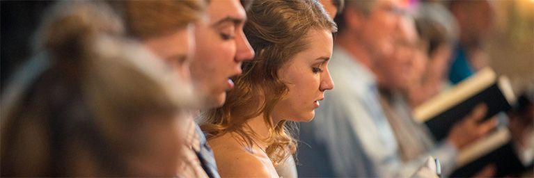 Bethany Lutheran College students in Minnesota stand close together, holding books and singing, with a soft focus highlighting their engagement.