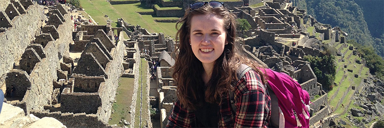 A woman with brown hair and a pink backpack smiles while standing in front of ancient stone ruins near Mankato, Minnesota.