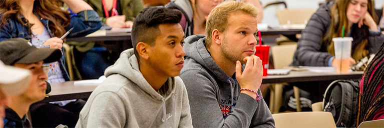 Students sit attentively in a Bethany Lutheran College classroom in Mankato, listening to a lecture with notebooks and drinks on their desks.