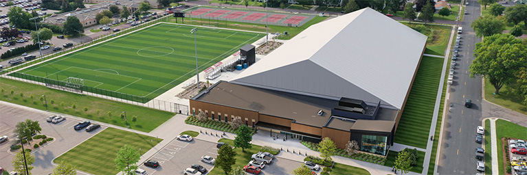 Aerial view of a Minnesota sports complex featuring a covered arena, multiple soccer fields, and tennis courts used for campus community events.