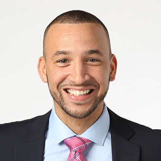 A man in a suit and pink tie smiles, representing the Mankato campus community, against a plain white background.