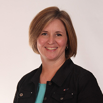 Smiling woman with short light brown hair, wearing a black jacket and teal top, representing the Bethany Lutheran College campus community.