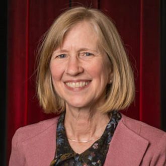 A smiling woman with shoulder-length blonde hair wearing a pink blazer, representing the Bethany Lutheran College campus community.