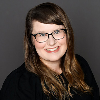 A smiling woman with glasses and long brown hair, wearing a black top, representing student engagement at Bethany Lutheran College.