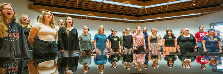 A group sings together next to a large, glossy table at Bethany Lutheran College in Mankato.